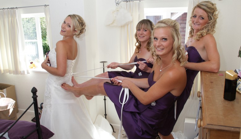 Bridesmaids helping the bride into her wedding dress